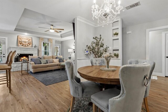 dining area with a tray ceiling, visible vents, light wood-type flooring, and ceiling fan with notable chandelier