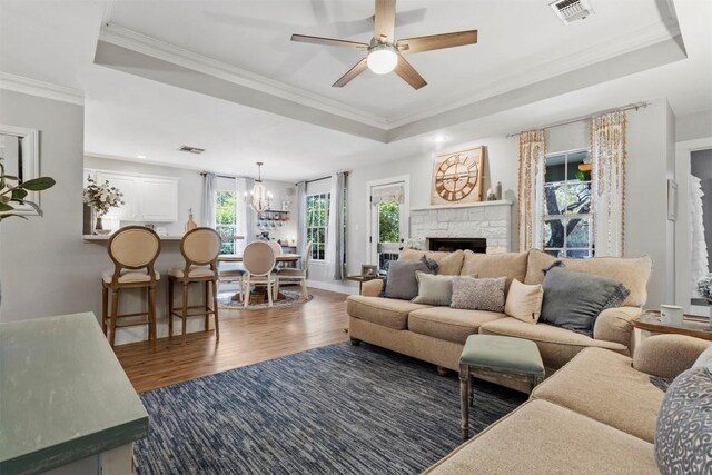 living room with a raised ceiling, crown molding, dark wood-style flooring, and visible vents