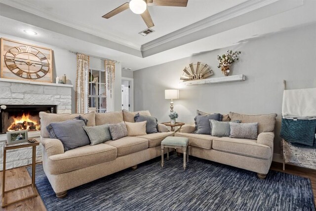 living room featuring a fireplace, crown molding, a ceiling fan, visible vents, and wood finished floors