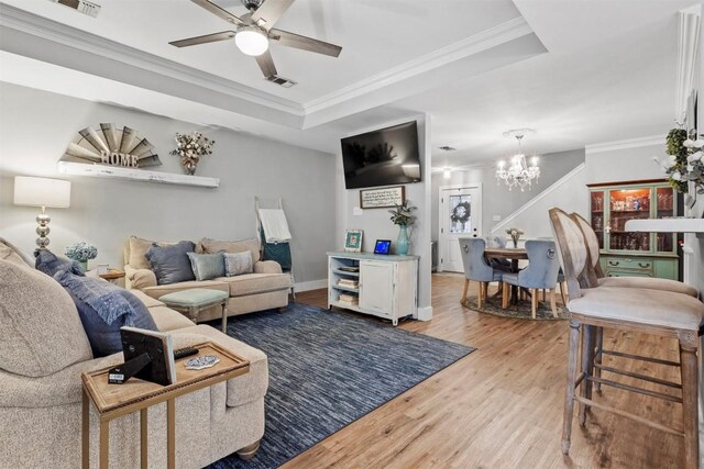 living room featuring visible vents, ornamental molding, a tray ceiling, wood finished floors, and ceiling fan with notable chandelier
