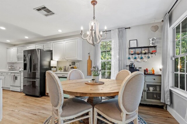 dining space with light wood-type flooring, a healthy amount of sunlight, an inviting chandelier, and visible vents