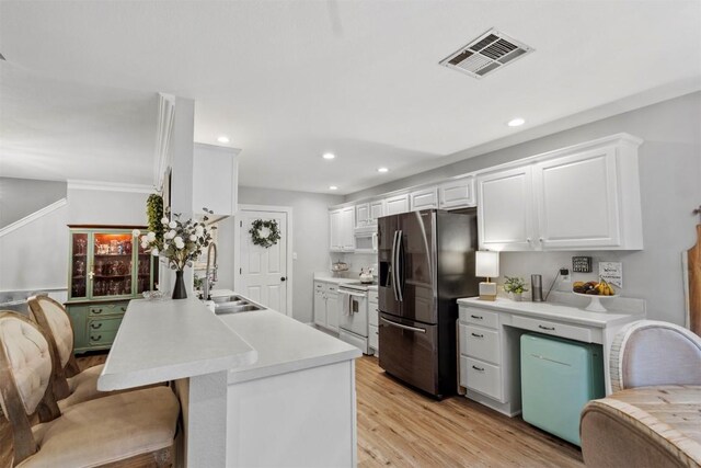 kitchen featuring a peninsula, stainless steel refrigerator with ice dispenser, visible vents, electric stove, and a sink