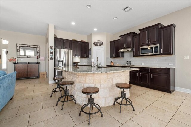 100 Adorno Ln, Georgetown, TX 78628 - kitchen featuring appliances with stainless steel finishes, a kitchen bar, backsplash, light stone countertops, and recessed lighting
