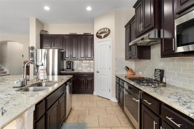 100 Adorno Ln, Georgetown, TX 78628 - kitchen with a sink, under cabinet range hood, appliances with stainless steel finishes, arched walkways, and light stone counters