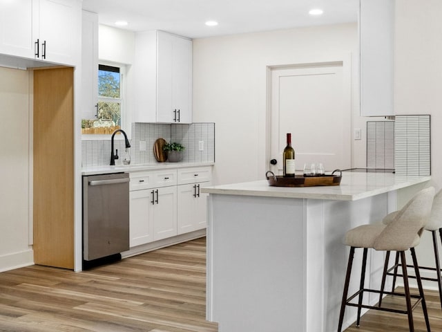 5416 Coventry Ln, Austin, TX 78723 - kitchen featuring stainless steel dishwasher, light wood finished floors, decorative backsplash, a kitchen breakfast bar, and white cabinetry