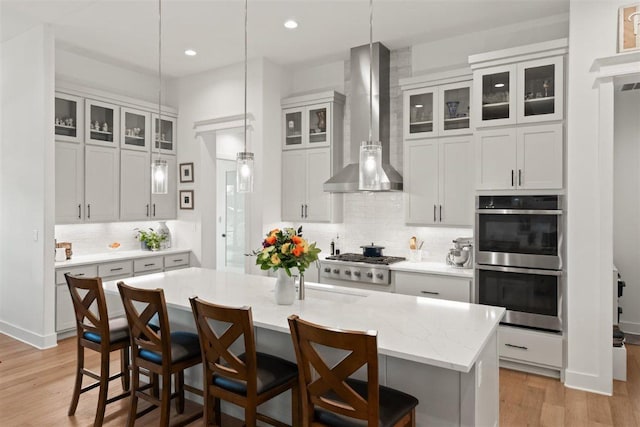 425 Private Road 915, Georgetown, TX 78633 - kitchen with wall chimney range hood, decorative backsplash, light wood-type flooring, a kitchen bar, and appliances with stainless steel finishes
