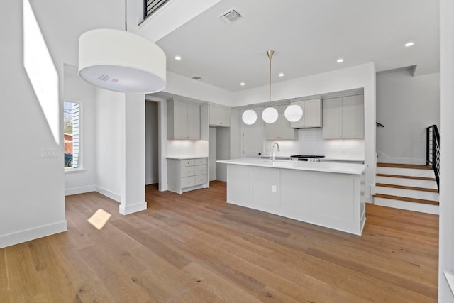 710 Philco Dr, Austin, TX 78745 - kitchen featuring light wood-style flooring, light countertops, tasteful backsplash, an island with sink, and gray cabinetry