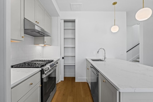 4525 S 3rd St, Austin, TX 78745 - kitchen featuring appliances with stainless steel finishes, under cabinet range hood, a peninsula, dark wood-style floors, and tasteful backsplash