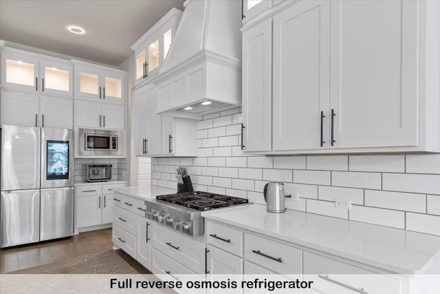 145 Gaston Dr, Bastrop, TX 78602 - kitchen with white cabinets, backsplash, glass insert cabinets, appliances with stainless steel finishes, and premium range hood