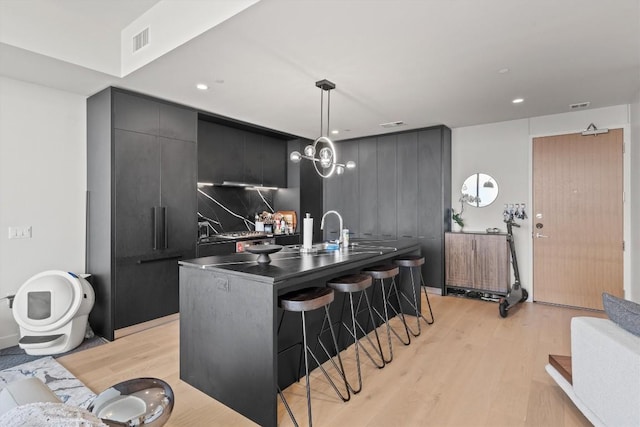 44 E Ave Unit 3402, Austin, TX 78701 - kitchen featuring a kitchen bar, light wood-type flooring, dark countertops, hanging light fixtures, and a center island with sink