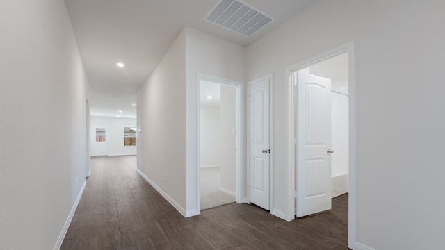 corridor featuring visible vents, baseboards, and dark wood-style floors
