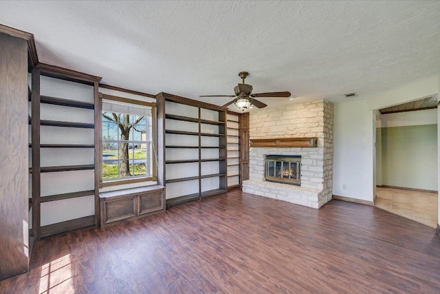 unfurnished living room featuring a textured ceiling, wood finished floors, ceiling fan, a brick fireplace, and baseboards