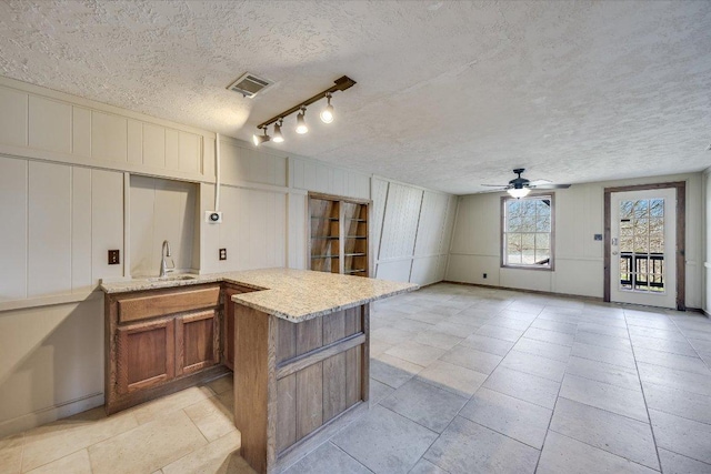 kitchen featuring brown cabinetry, a sink, a ceiling fan, a decorative wall, and a textured ceiling