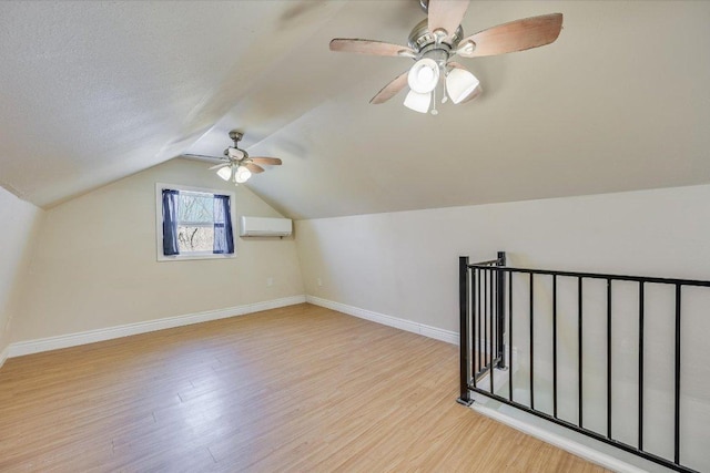 bonus room with an AC wall unit, wood finished floors, baseboards, ceiling fan, and lofted ceiling