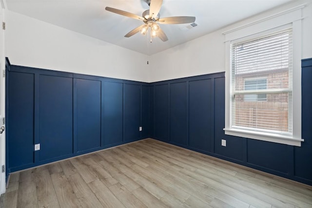 unfurnished room with light wood-type flooring, a decorative wall, a wainscoted wall, visible vents, and a ceiling fan