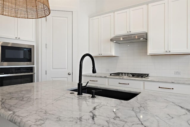 kitchen featuring white cabinetry, under cabinet range hood, decorative backsplash, a sink, and appliances with stainless steel finishes