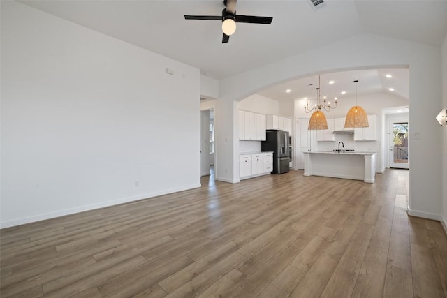 unfurnished living room featuring light wood finished floors, baseboards, arched walkways, ceiling fan with notable chandelier, and vaulted ceiling