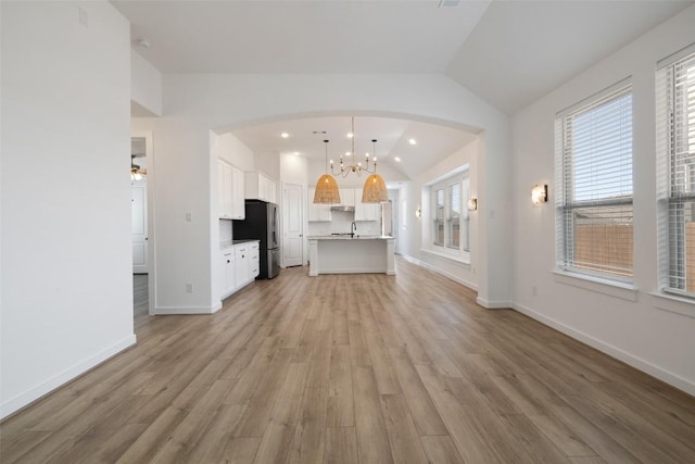 unfurnished living room with a sink, lofted ceiling, light wood-style flooring, baseboards, and arched walkways