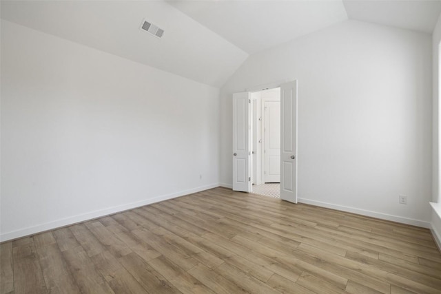 spare room featuring baseboards, visible vents, light wood-style flooring, and lofted ceiling
