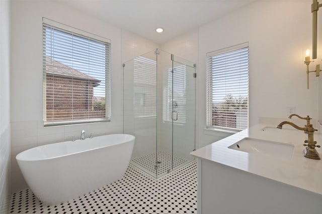 full bath featuring tile walls, a shower stall, double vanity, a sink, and a freestanding bath