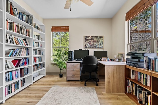 home office with a ceiling fan, wood finished floors, and wall of books