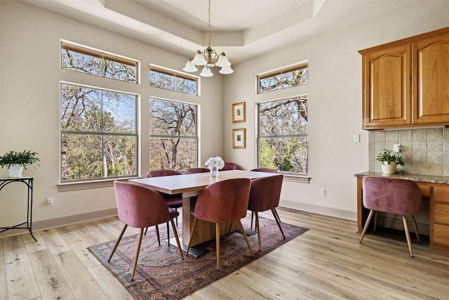 dining space featuring a raised ceiling, a high ceiling, a chandelier, and light wood-type flooring