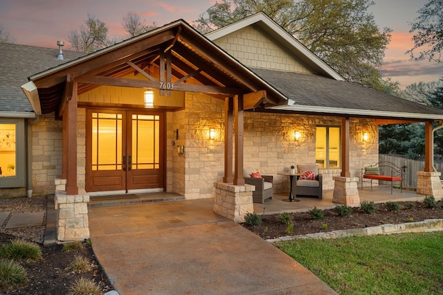 7603 Rustling Cv, Austin, TX 78731 - exterior entry at dusk with stone siding, roof with shingles, a porch, and an outdoor hangout area