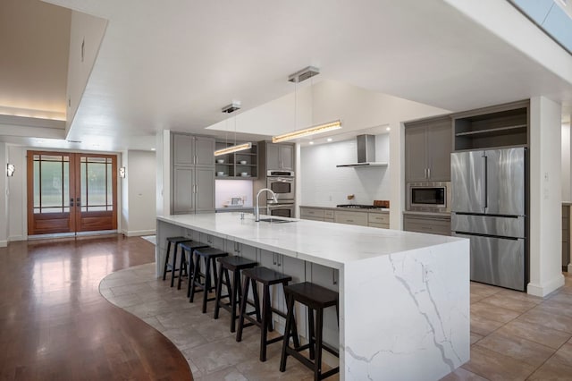7603 Rustling Cv, Austin, TX 78731 - kitchen featuring appliances with stainless steel finishes, open shelves, gray cabinets, tasteful backsplash, and wall chimney range hood
