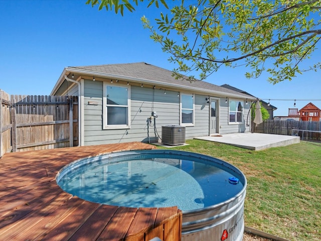 view of swimming pool featuring central AC unit, a fenced backyard, a wooden deck, a jacuzzi, and a yard