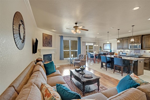 living room with ceiling fan, ornamental molding, a glass covered fireplace, a textured wall, and recessed lighting