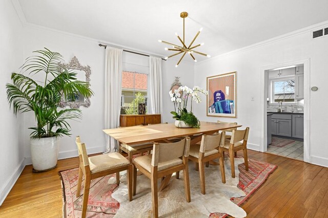 dining area featuring light wood finished floors, visible vents, crown molding, and an inviting chandelier