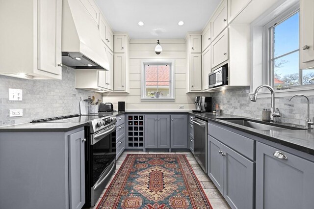 kitchen with stainless steel appliances, gray cabinets, a sink, decorative backsplash, and custom exhaust hood