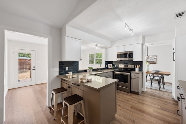 125 Chaparral St, San Marcos, TX 78666 - kitchen featuring stainless steel appliances, a sink, light wood-type flooring, a kitchen breakfast bar, and a textured ceiling