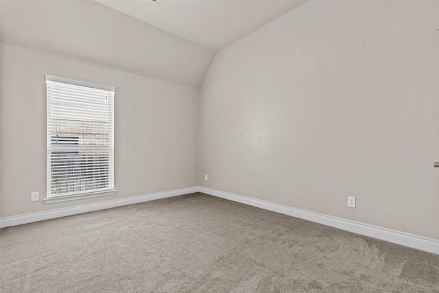 empty room featuring carpet flooring, baseboards, and vaulted ceiling