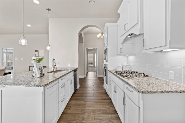 kitchen featuring decorative backsplash, stainless steel appliances, arched walkways, white cabinetry, and a sink