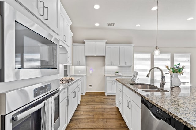 kitchen with dark wood-style flooring, stainless steel appliances, backsplash, a sink, and white cabinets