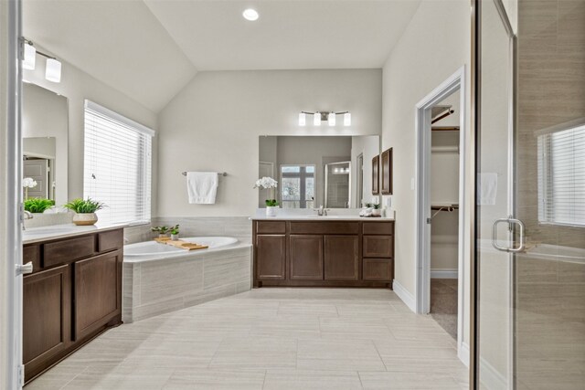bathroom featuring a shower stall, lofted ceiling, two vanities, and a garden tub