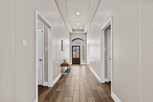 corridor featuring a textured wall, baseboards, and wood tiled floor