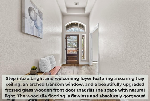 foyer with a textured wall, a tray ceiling, visible vents, and wood finished floors