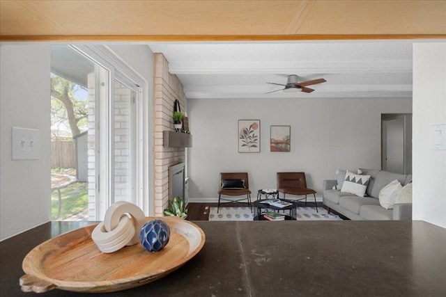 living room featuring ceiling fan, a brick fireplace, and beam ceiling