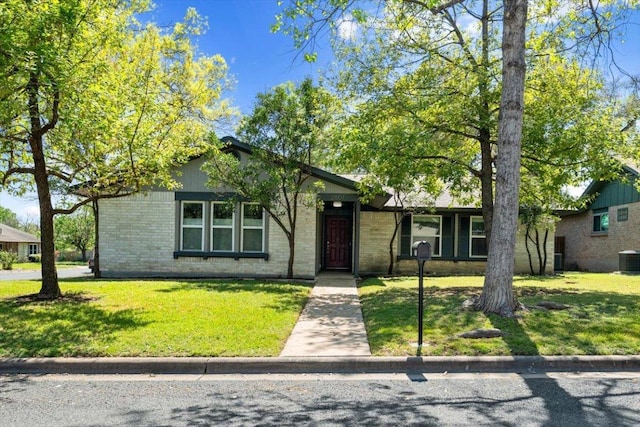 view of front facade with central air condition unit, brick siding, and a front yard