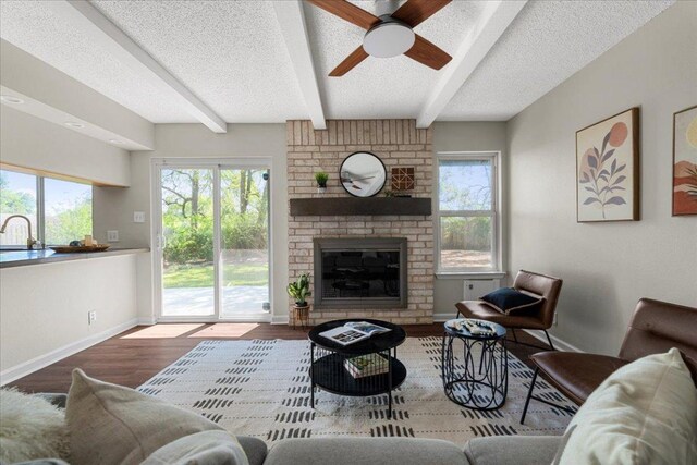 living area with ceiling fan, a textured ceiling, a fireplace, beam ceiling, and baseboards