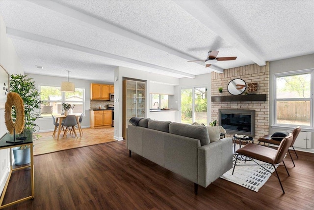 living room featuring beam ceiling, a fireplace, ceiling fan, a textured ceiling, and dark wood finished floors