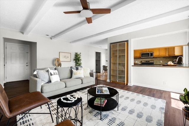 living room with a ceiling fan, a textured ceiling, wood finished floors, and beamed ceiling