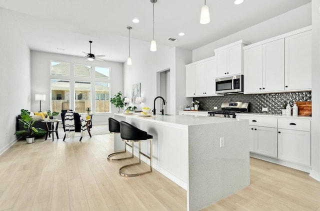 2316 Gold Dust Trl, Leander, TX 78641 - kitchen featuring appliances with stainless steel finishes, a ceiling fan, backsplash, light wood-style floors, and a kitchen island with sink