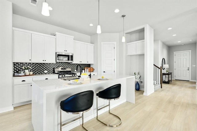 2316 Gold Dust Trl, Leander, TX 78641 - kitchen featuring stainless steel appliances, light wood-style floors, tasteful backsplash, white cabinets, and decorative light fixtures