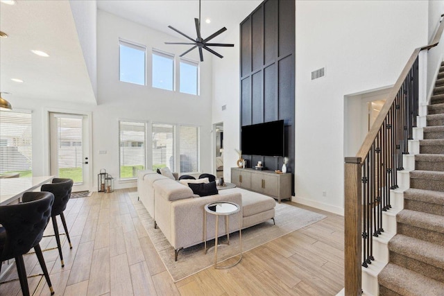 living area featuring light wood-type flooring, visible vents, a high ceiling, and stairs
