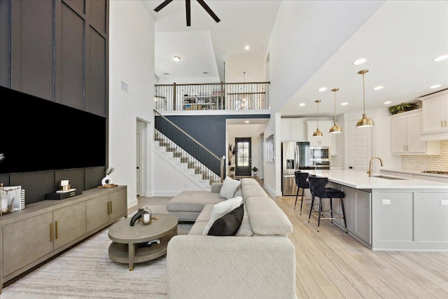living area featuring a ceiling fan, stairs, a towering ceiling, light wood finished floors, and recessed lighting