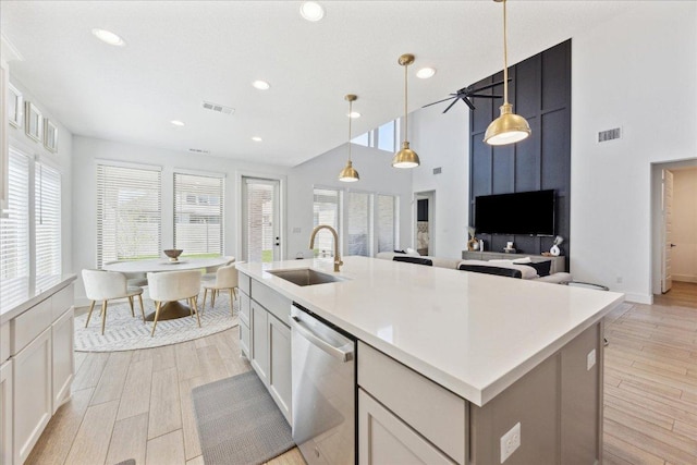 kitchen featuring light wood finished floors, an island with sink, dishwasher, visible vents, and a sink