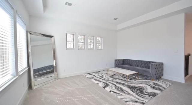 living area with a raised ceiling, visible vents, carpet flooring, and baseboards